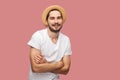 Portrait of happy successful bearded young man in white shirt with hat standing, crossed arms and looking at camera with toothy Royalty Free Stock Photo