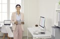 Happy smiling company worker or businesswoman standing in office with computer desks Royalty Free Stock Photo