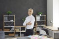 Happy confident successful senior businessman standing by office desk and smiling