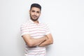 Portrait of happy successful handsome bearded young man in striped t-shirt standing with crossed arms and looking at camera with Royalty Free Stock Photo