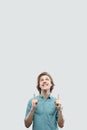 Portrait of happy toothy smiley handsome long haired blonde young man in blue casual shirt standing and pointing at up copyspace Royalty Free Stock Photo