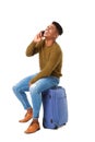 Happy travel man sitting talking with cellphone and sitting on suitcase against isolated white background Royalty Free Stock Photo