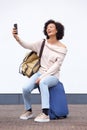 Happy travel woman sitting on suitcase and taking selfie against white wall Royalty Free Stock Photo