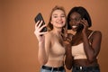Portrait of a happy two smiling international girls making selfie photo on smartphone and showing two fingers sign on Royalty Free Stock Photo