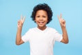 Portrait of happy and victorious little boy in T-shirt showing victory or peace gesture and smiling, doing v sign