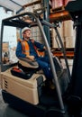 Portrait of a happy warehouse worker sitting in forklift truck at large warehouse