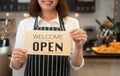 Portrait of a happy woman Asian waitress standing at a coffee shop holding open sign while reopening care during coronavirus Royalty Free Stock Photo