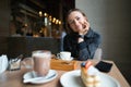 Portrait of a happy woman eating a piece of cake and drinking coffee while sitting at the table in a cafe indoors Royalty Free Stock Photo