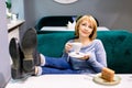 Portrait of a happy woman eating a piece of cake and drinking coffee while sitting at the table in a cafe indoors Royalty Free Stock Photo