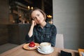 Portrait of a happy woman eating a piece of cake and drinking coffee while sitting at the table in a cafe indoors Royalty Free Stock Photo