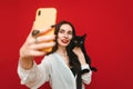 Portrait of happy woman in light clothing taking selfie with black cat on smartphone, hugging pet and looking into smartphone Royalty Free Stock Photo