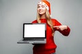 Portrait of a happy woman in a red sweater and Santa Claus hat, showing a blank laptop screen and pointing her finger at him, look Royalty Free Stock Photo