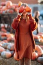Portrait of happy woman with ripe orange pumpkins in hands close eyes near wagon with orange pumpkin on farmers market in brown