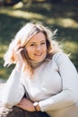 Portrait of happy woman sitting in autumn city park on sunny day closeup. Adult lady in casual clothes relaxing among