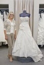 Portrait of a happy woman standing by elegant bridal dress in boutique Royalty Free Stock Photo