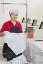 Portrait of a happy woman wearing uniform holding clothes with washing machines in background