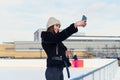 Portrait of a happy woman in winter cloth making selfie photo on smartphone while skating on the ice rink. Royalty Free Stock Photo