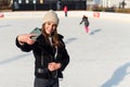 Portrait of a happy woman in winter cloth making selfie photo on smartphone while skating on the ice rink. Royalty Free Stock Photo