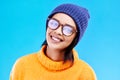 Portrait of happy woman in winter fashion with glasses, beanie and smile isolated on blue background. Style, happiness Royalty Free Stock Photo