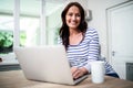 Portrait of happy woman working on laptop while holding coffee mug Royalty Free Stock Photo