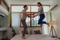 Portrait of happy young adult Asian couple jumping on bed together in bedroom interior scene. 30s mature husband and Royalty Free Stock Photo