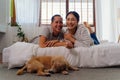 Portrait of happy young adult Asian couple looking at camera on bed together with dog pet in bedroom interior scene. 30s Royalty Free Stock Photo