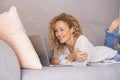 Portrait of happy young adult womn using computer laying down on the couch at home in indoor relaxation leisure acitivy alone. Royalty Free Stock Photo