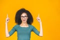 Portrait of a happy young african american curly woman pointing fingers up at copy space isolated over yellow background Royalty Free Stock Photo