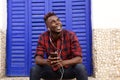 Happy young african man sitting outdoors with mobile phone and looking away Royalty Free Stock Photo