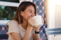 Portrait of happy young asian business woman with mug in hands drinking coffee in the morning at cafe. Royalty Free Stock Photo