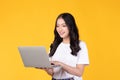 Portrait of happy young Asian businesswoman, student in white t-shirt working on silver laptop computer isolated on yellow Royalty Free Stock Photo