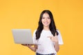 Portrait of happy young Asian businesswoman, student in white t-shirt working on silver laptop computer isolated on yellow Royalty Free Stock Photo