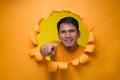 Portrait of Happy young Asian man pointing forward, looking at camera, poses through torn paper hole Royalty Free Stock Photo