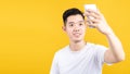 Portrait happy young asian man taking selfie with mobile phone camera smiling with copy space wearing white t-shirt on yellow back Royalty Free Stock Photo