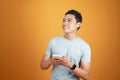 Portrait of a happy young asian man using mobile phone at studio on orange background Royalty Free Stock Photo