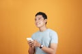 Portrait of a happy young asian man using mobile phone at studio on orange background Royalty Free Stock Photo