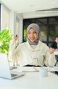 Happy Asian Muslim female office worker hands up, celebrating her success, project approved Royalty Free Stock Photo