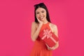 Portrait of a happy young asian woman holding gift box isolated over pink background. dressed in orange dress and sunglasses on Royalty Free Stock Photo