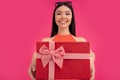 Portrait of a happy young asian woman holding gift box isolated over pink background. dressed in orange dress and sunglasses on Royalty Free Stock Photo