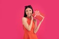 Portrait of a happy young asian woman holding gift box isolated over pink background. dressed in orange dress and sunglasses on Royalty Free Stock Photo