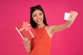 Portrait of a happy young asian woman making selfie with gift box isolated over pink background. dressed in orange dress and Royalty Free Stock Photo