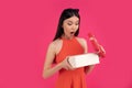 Portrait of a happy young asian woman shocked open gift box isolated over pink background. dressed in orange dress and sunglasses Royalty Free Stock Photo