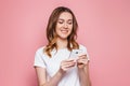 Portrait of a happy young ÃÂaucasian woman in a white T-shirt using mobile phone  over pink background, girl student with Royalty Free Stock Photo