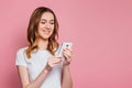 Portrait of a happy young ÃÂaucasian woman in a white T-shirt using mobile phone  over pink background, girl student with Royalty Free Stock Photo