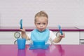 Portrait Of Happy Young Baby Boy in a blue bib with fork and knife in his hands In High Chair in the modern kitchen