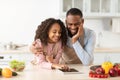 Black man and girl cooking in kitchen using digital tablet Royalty Free Stock Photo