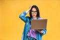 Portrait of happy young beautiful surprised amazed shocked woman with glasses standing with laptop isolated on yellow background. Royalty Free Stock Photo