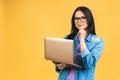 Portrait of happy young beautiful surprised woman with glasses standing with laptop isolated on yellow background. Royalty Free Stock Photo