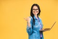 Portrait of happy young beautiful surprised woman with glasses standing with laptop isolated on yellow background Royalty Free Stock Photo