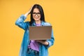Portrait of happy young beautiful surprised woman with glasses standing with laptop isolated on yellow background Royalty Free Stock Photo
